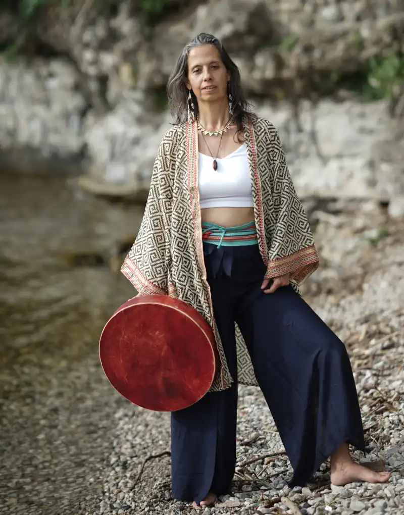 Camille Barrios standing by a lake with her red shamanic drum